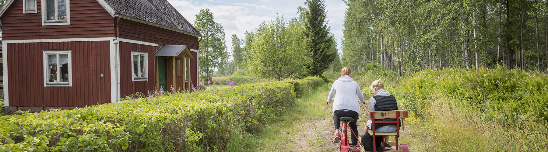 Människor cyklar förbi röd stuga