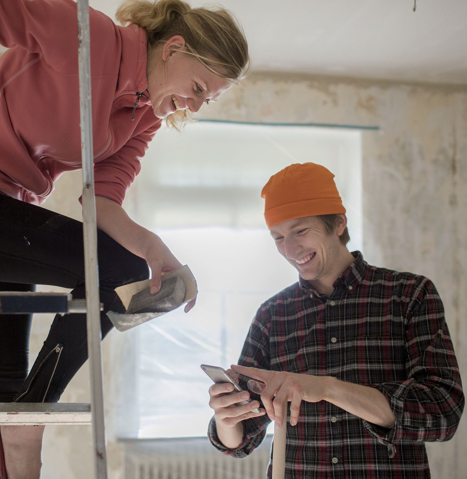 Kvinna på stege och man med mössa håller i telefon