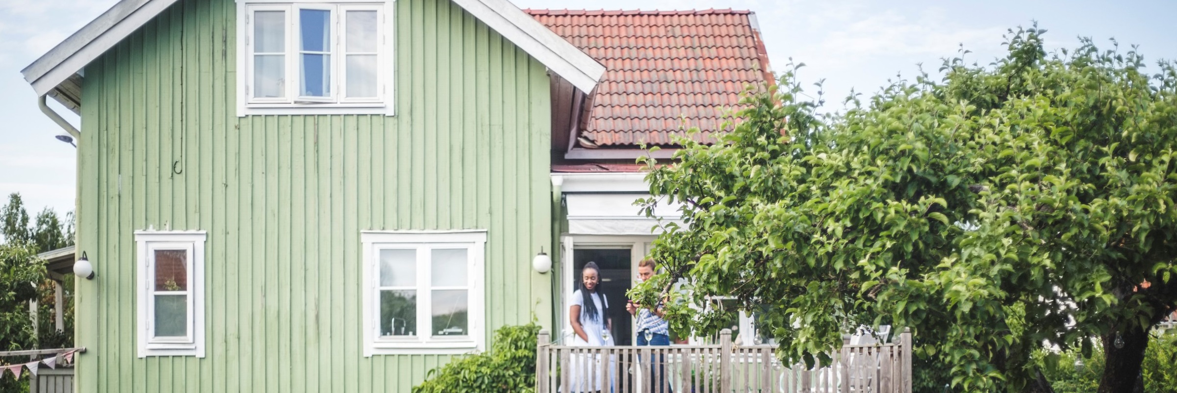 Par pratar på veranda utanför grönt hus
