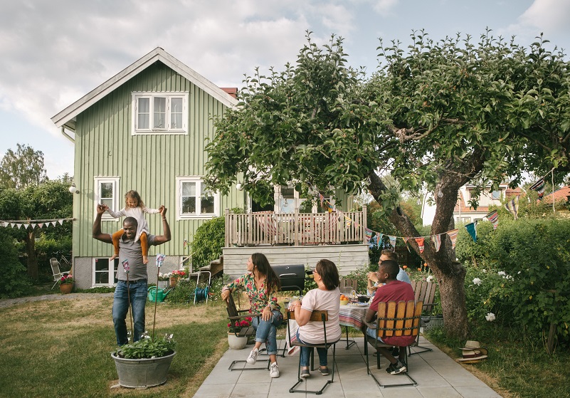 Familj i trädgården sitter i trädgårds medan dotter medan dotter sitter på pappas axlar