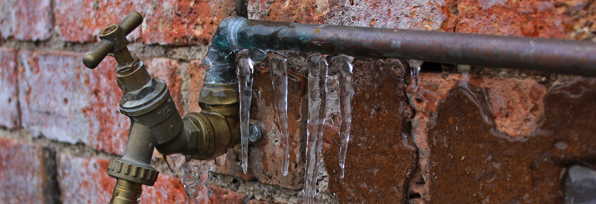 Fruset vattenrör och kran mot tegelvägg